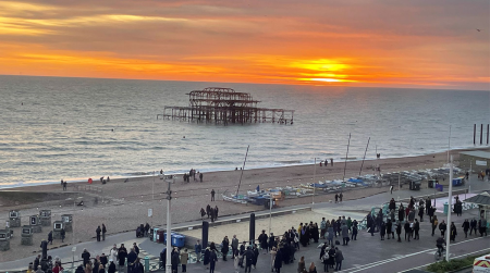 Sunsetting behind west pier on Brighton sea front with graduates on promenade