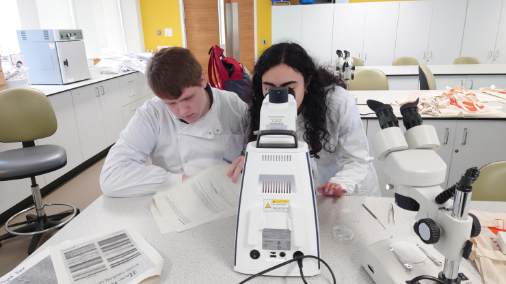 Two young people in a lab in white lab coats using a microscope