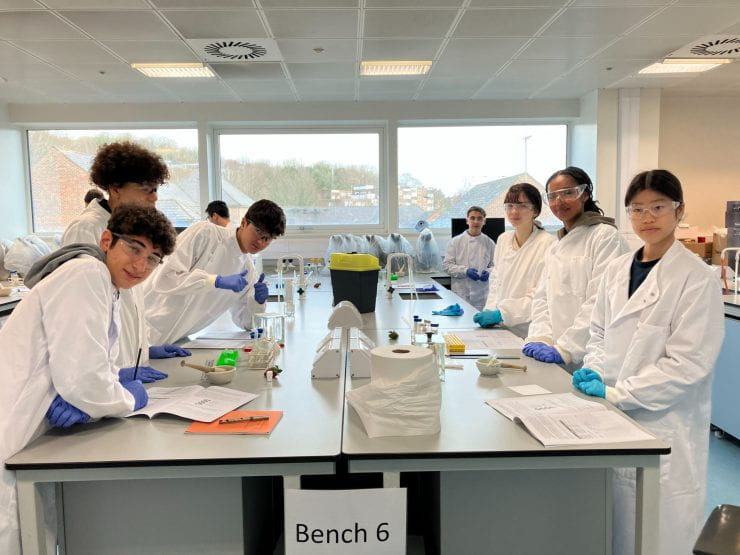Group of school students wearing safety goggles and white lab coats in a lab