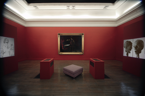 Gallery installation photograph, dark red walls with white decal, photographic images of Cromwell's skull head and drawing of the beheading of Charles I. Centre, Delaroche’s painting of Cromwell contemplating the beheaded corpse of Charles 1st in his coffin after execution in 1649.