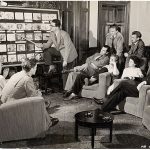 Animators' meeting 1940s suits, seven men one woman in armchairs watching a presenter at a board of animation stills