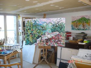 Studio picture of a crowded space with large landscape on central easel and French windows