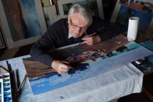 Ian Potts with glasses and grey hair, adding detail to a large watercolour of Hastings beach.