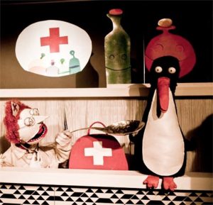 Puppets staged as doctor and patient, a tall penguin takes medicine on a spoon from a ball-headed doctor