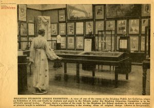 Yellowed newspaper cutting shows gallery space with hung pictures, vitrines and a flowing dress on a mannequin. Reads: Brighton students' unique exhibition, a view of one of the rooms at the Brighton Public Art Galleries where an exhibition of arts and crafts is to be officially opened today.