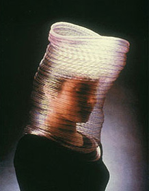 Fashion photograph of cylindrical headdress covering whole head and shoulders in plastic gauze