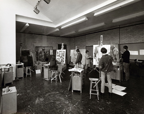 Black and white photograph. Large space with 1950s designed ceiling. Students standing at easels painting.