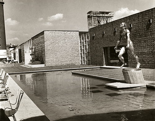 Black and white image of a male figure statue standing over an outdoor fountain area outside the Homes and Gardens Pavilion at the Festival of Britain, 1951. Architects: Bronek Katz and Reginald Vaughan. Taken from the Design Council Archive housed at the University of Brighton Design Archives.