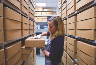 A colour photograph of Sue Breakell looking at archival boxes at the University of Brighton Design Archives