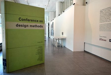 Gallery view showing giant green book titled 'Conference on design methods' on left side of image. The right side shows exhibition test , display table and framed images on the wall.