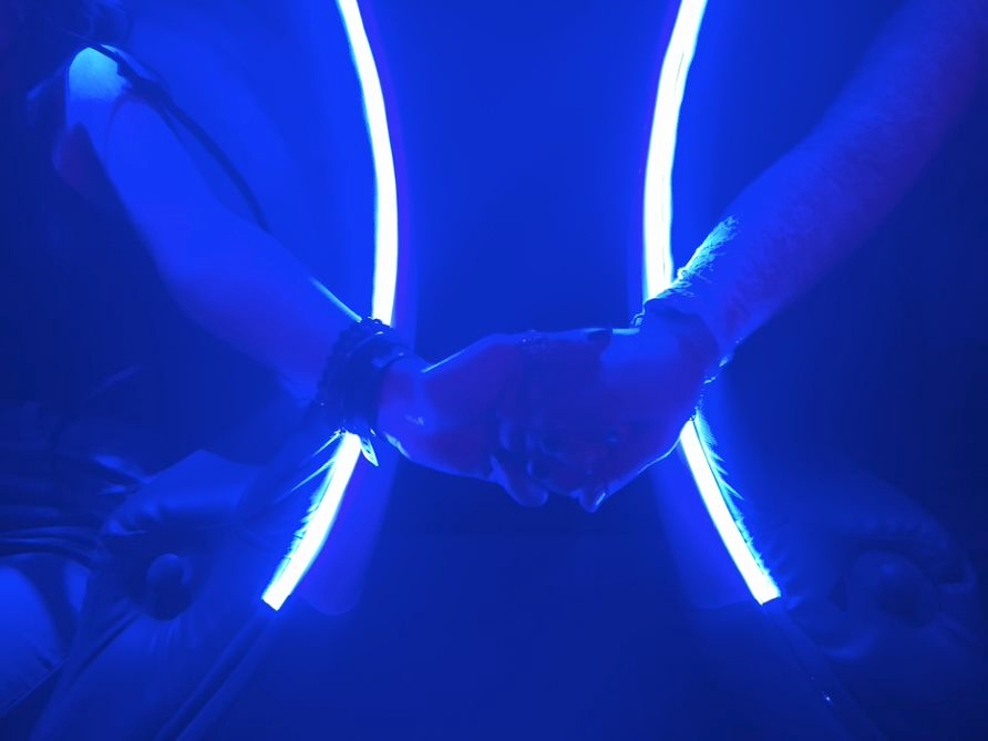Two people holding hands (you can only see their arms) With neon blue lights behind them.