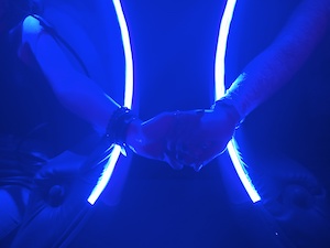 Two hands holding across a blue screen with uv lights behind them