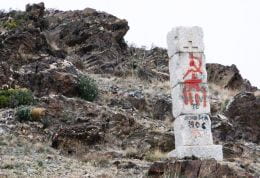 Rocky slope with monument built of five stones. Has an embossed Christian cross and, graffitied, date 1906 and the hammer and sickle symbol