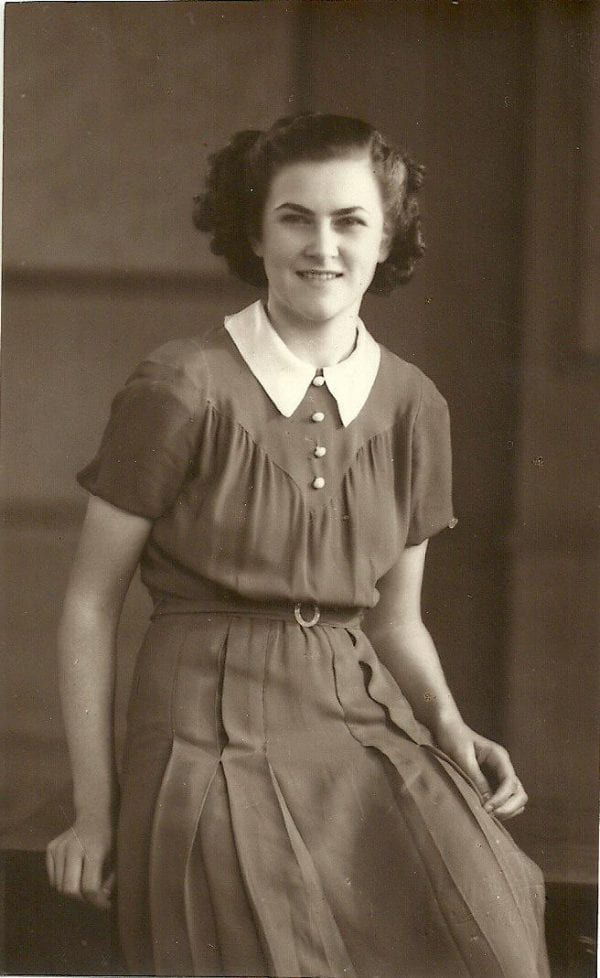 Sepia tinted three quarter length portrait of young woman in smart casual dress circa 1940s and tied back hair seated on a desk