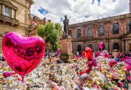 A town square with large pink heart balloons and a mass of Sellophane wrapped flowers. Middle distance, a statue on a plinth.