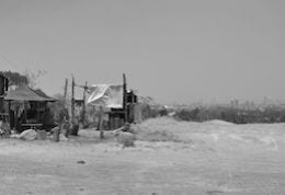 Arid landscape with small dwelling and distant city, black and white photograph