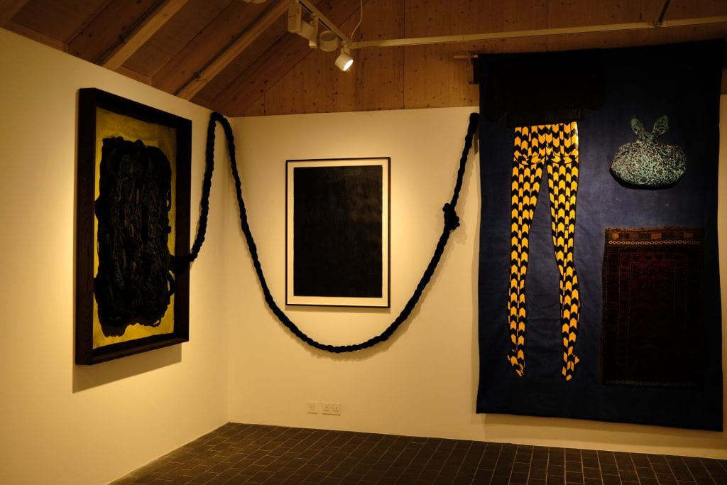 two large scale textile pieces connected by a large black plait with a smaller framed piece in the middle