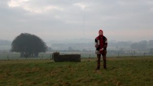 A person in wintry clothes stands in a field in a misty, rural landscape.