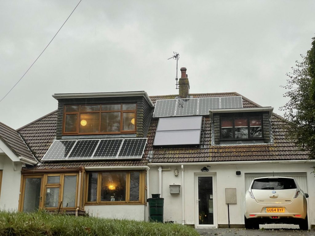 house with eight solar panels and two flat plate thermal panels on the roof. electric car in foreground.