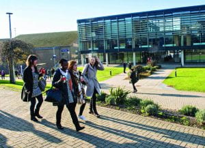 Group of students walking across Falmer campus in sunshine