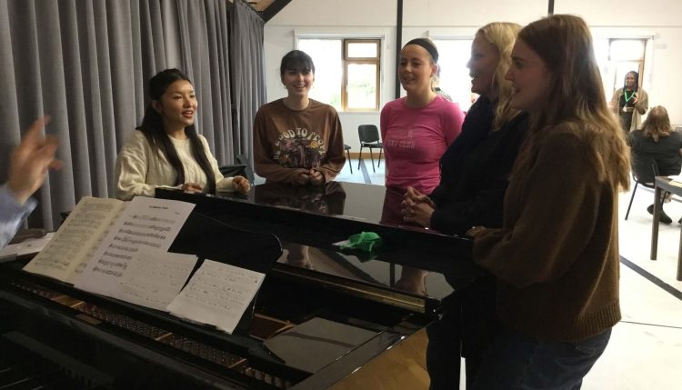 group of art and Design PGCe trainnes standing a round a piano singing