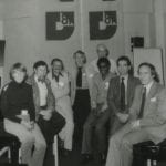 Group of eight people sitting in front if banners