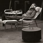 A man with headphones sitting on metal framed lounge chair with other metal furniture surrounding him