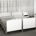 Black and white photo of bedroom setting with two white-ended single beds and a dressing table with mirror