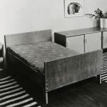 A black and white photo of a bedroom setting with double bed and low drawers