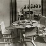 A dining room setting with a round table, chairs and drinks trolley