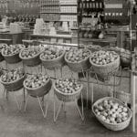 A black and white photo of an interior view of a grocery shop and its fruit display