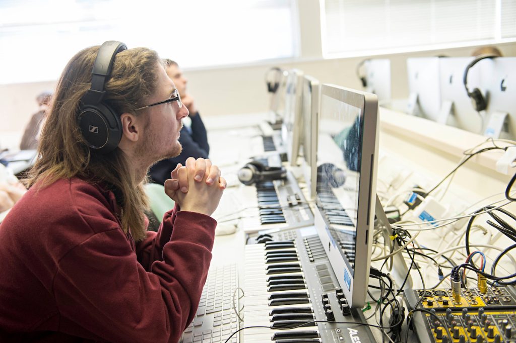 University student wearing headphones working on a computer with a mixing deck and recording equipment