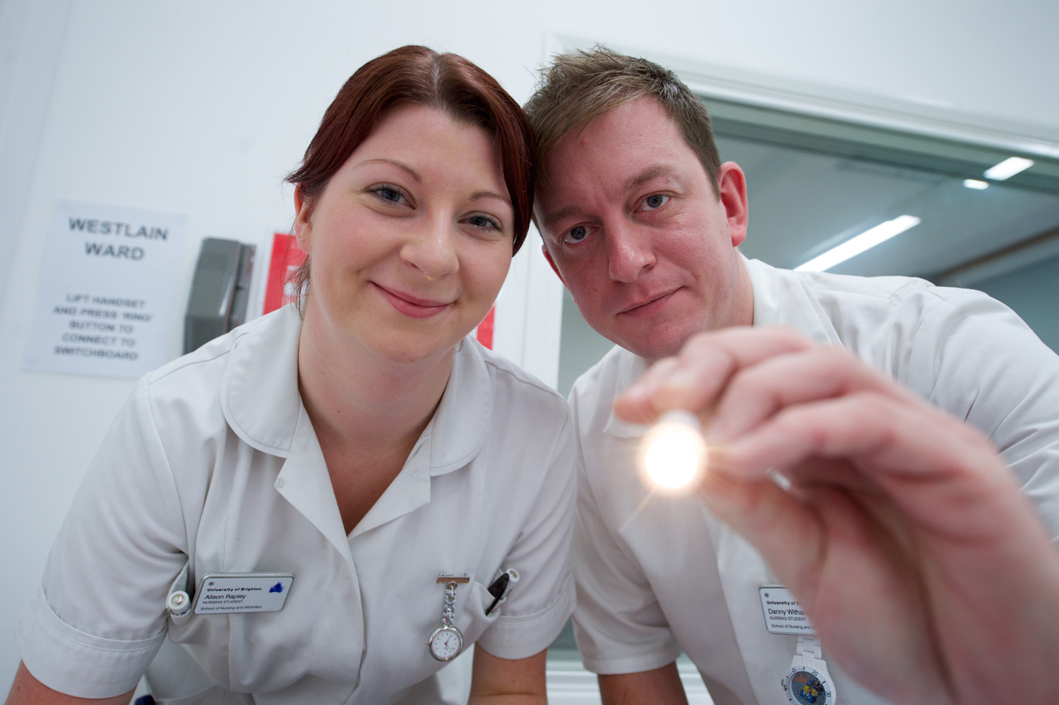 Two student nurses with a torch looking at the camera in a clinical setting