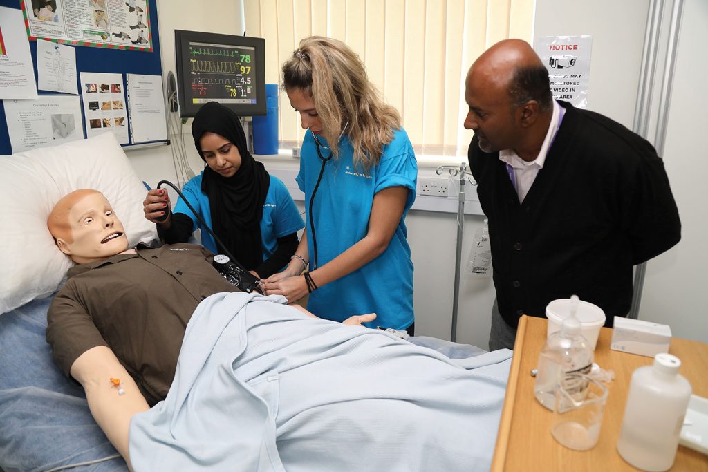 Two student nurses practicing clinical skills on a mannequin under supervision of a lecturer