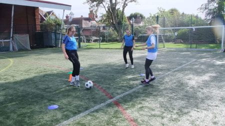 three female students dribbling with a football