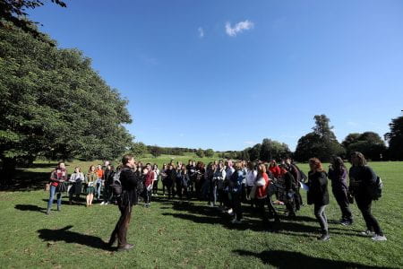 The image is of a man addressing a crowd of students in a countryside setting