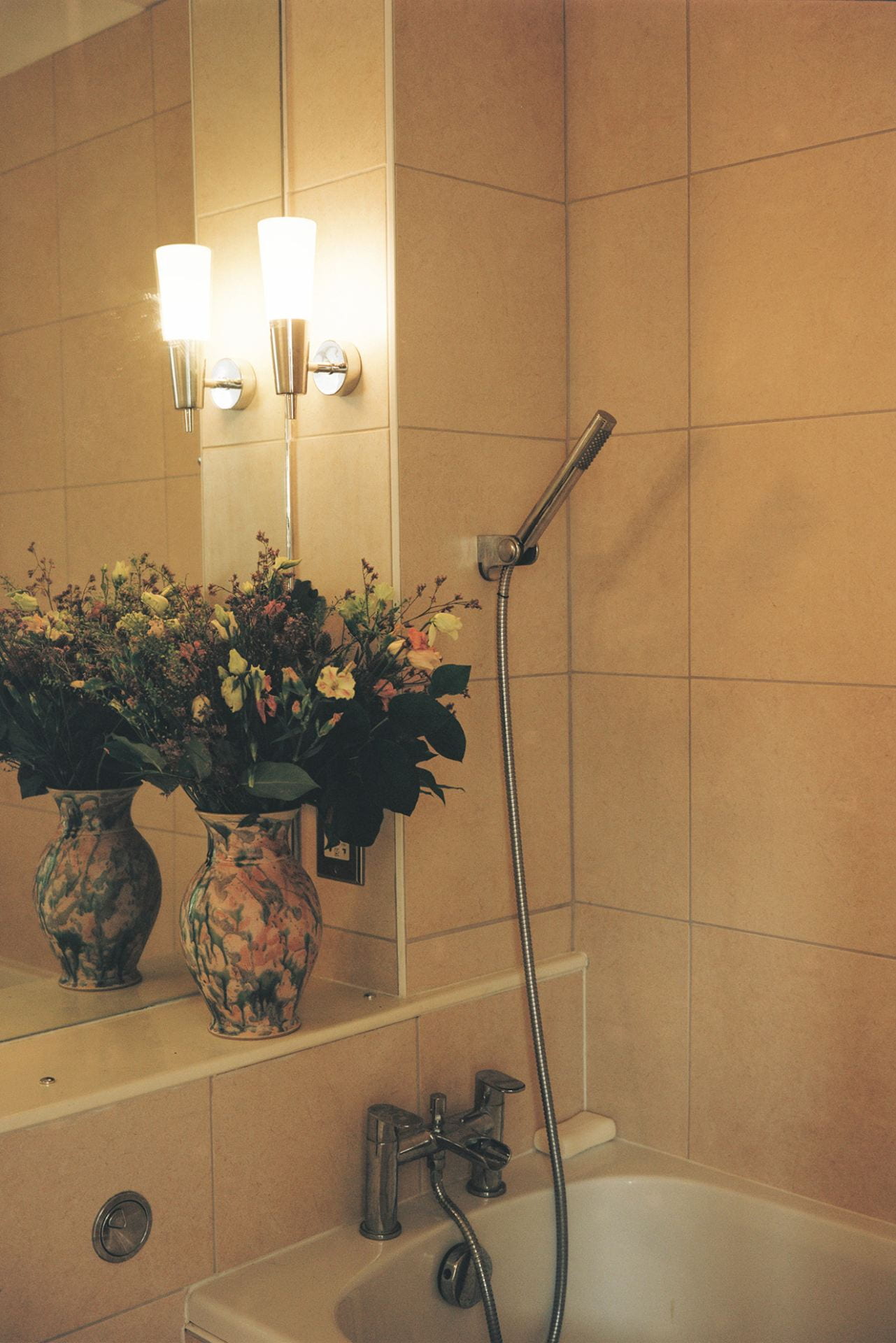 photograph of a bathrrom with a showerhead and a vase of flowers