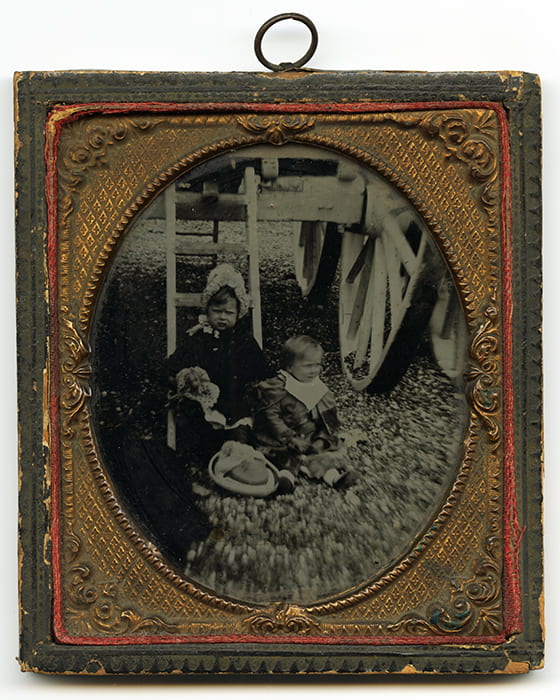 A black and white portrait of two children, encased in an elaborate gold and red frame