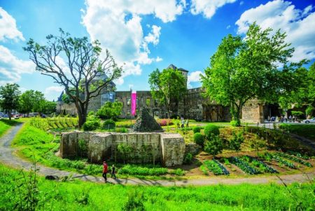 Stone walls of a castle are surrounded by rows of vegetables and a public pathway. (Source: Urban Green Blue Grids, 2022)