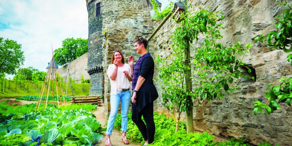 Two people stand eating fruit next to a stone wall amongst growing vegetables. (Source: Urban Green Blue Grids, 2022)