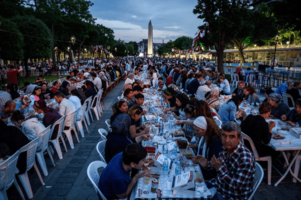 Hundreds of people sit at long tables eating a Iftar dinner
