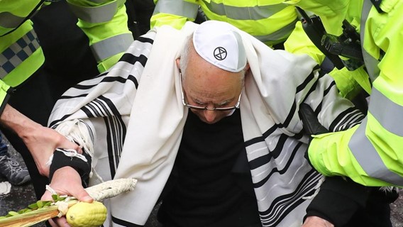 Rabbi Jeffrey Newman holding lulav and etrog wearing a tallit, a prayer shawl and kippah, skull cap with XR logo on it being arrested by police