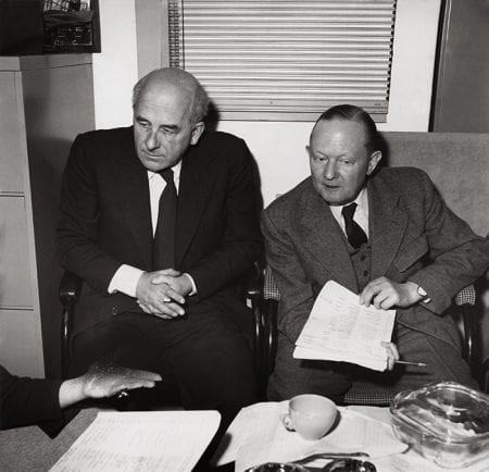 Black and white portrait of Milner Gray sitting down with another man over a pile of papers
