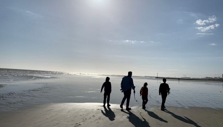 Image of man and three children walking across a beach in silhouette.