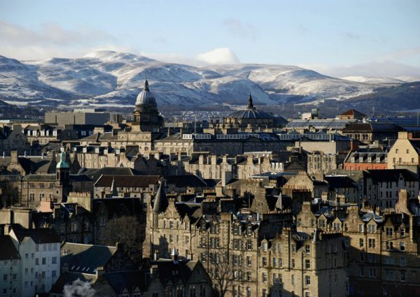 Edinburgh city scape with dark brick, domes and snow-capped hills beyond.