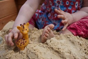 Girl playing in sandpit with a toy giraffe