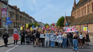 Large group of marchers on Lewes Rd, Brighton. Photo of front of march, with large banner "Support Our Staff"